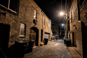 Dark and eerie urban city cobblestone brick paved alley at night