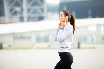 Pretty young sportswoman putting on headphones and listening to music in city