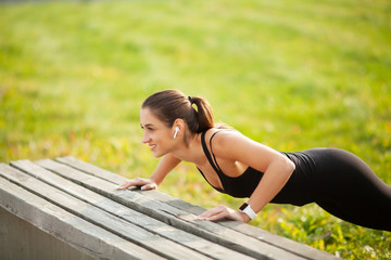 Portrait of beautiful sporty woman 20s in sportswear doing push-ups, and listening to music with...