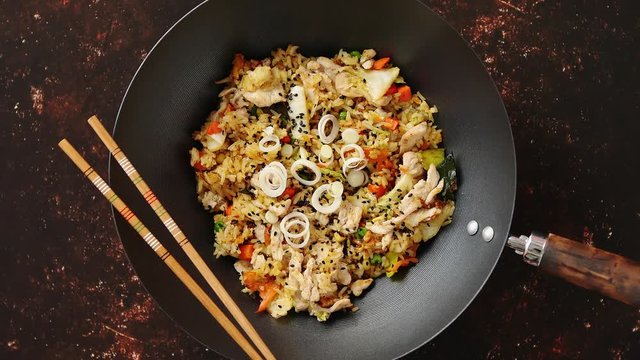 Delicious fried rice with chicken. Prepared and served in a wok with soy and sweet sour souces on side. Placed on dark rusty background. Top view.