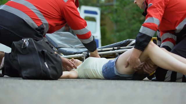 Ambulance service staff taking unconscious girl to ambulance, using stretcher