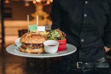 Big tasty burger with fresh salad served by waiter with black costume - Powered by Adobe