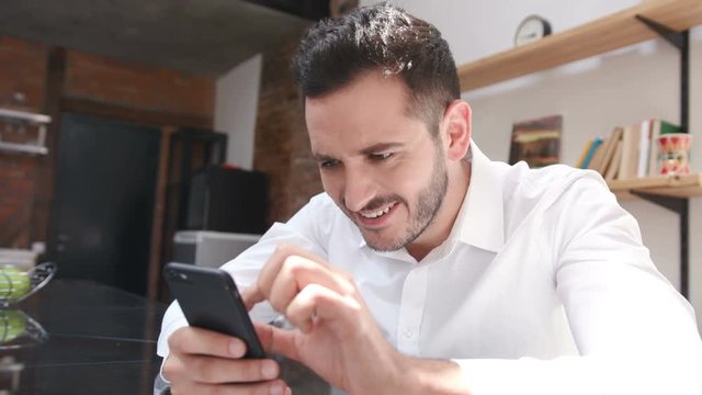 Fabulous positive man touching screen of smartphone, looking at image. Portrait of surprised nice guy with beard. Indoors. Close-up.