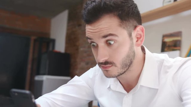 Terrific young man in seeing something impressive in social media. Funny surprised guy with big green eyes looking into camera. Close-up. Indoors. Portrait.