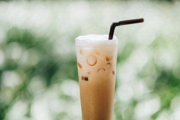 Glass with cold latte macchiato on table in the garden. Blur garden background