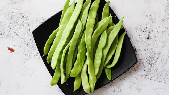 Black ceramic plate with fresh green bean pods placed on white rusty table. Top view shot with copy space.
