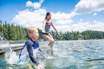 A little boy and little girl jumping off the dock into a beautiful mountain lake. Having fun on a summer vacation. Splashing and getting wet