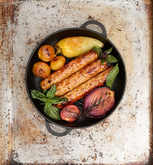 grilled juicy sausages in a pan on a gray background.
