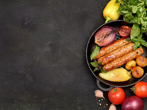 grilled juicy sausages in a pan on a black background