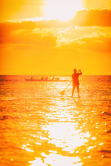Hawaii ocean lifestyle - watersport activity on ocean - stand up paddleboard, people training on outrigger canoe . Active summer healthy living. Silhouette of standing person doing paddle board.