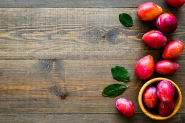Summer harvest of red plum.  Red plum and leaves pattern on dark wooden background top view copy space