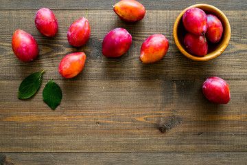 Plums on dinning table. Fresh raw red plum in wooden bowl on wooden background top view copy space