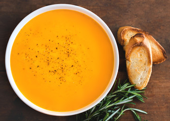 Pumpkin and carrot  Cream soup on rustic wooden table. Autumn Pumpkin cream-soup with rosemary herb and croutons. Top view. Copy space.