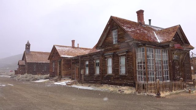 Decaying wooden houses of scenic Bodie, Nevada weathering the harsh winter conditions. Snowstorm slowly covering the ghost town and tranquil countryside in a remote part of USA. Cool wooden buildings.
