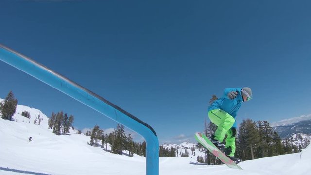LOW ANGLE: Male snowboarder slides down a metal railing in a scenic ski resort. Cinematic shot of extreme rider doing a cool grind trick while snowboarding in Squaw Valley. Man enjoying winter holiday