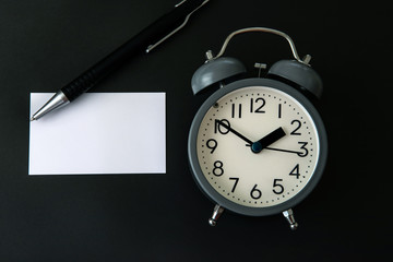 Time concept with a blank white paper note copy space to add wording or message , alarm clock with black pen decoration on black background