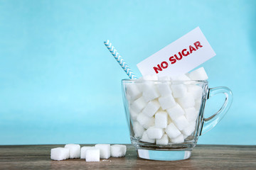 White sugar cube in glass and NO SUGAR tag label on a wooden table with light blue background , unhealthy sweet food concept for 14th November campaign of World Diabetes Day