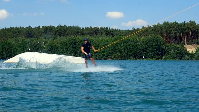 A wakeboarder slides over the water past the camera in a cable park. Slow motion