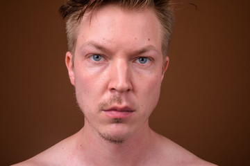 Fototapeta premium Young handsome man shirtless while grooming against brown backgr