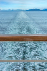 Straight line of ship's wake and wooden railing at stern.