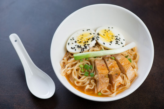 Ramen noodles with roasted chicken and egg served in a whiye bowl over dark brown metal background, studio shot