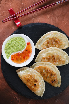 Above view of fried potstickers with dipping sauces on a stone slate tray, vertical shot