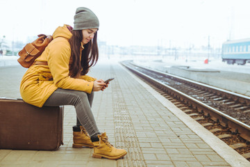 woman wait for train on railway station. travel concept. surfing internet on phone to kill time
