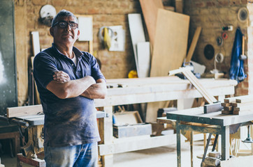 Portrait of senior carpenter. Standing in his workshop and looking at camera.