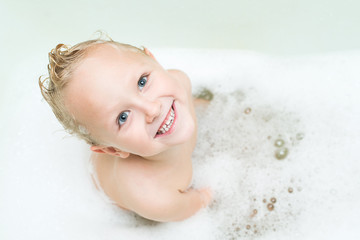 Happy baby bathes in the bathroom with foam