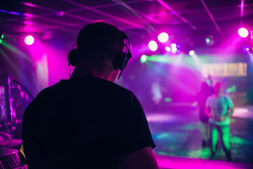 Fototapeta na wymiar DJ mixes music in a nightclub with people dancing on the dance floor