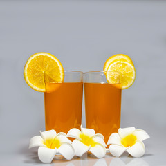 Two glasses of orange drink with orange slices and plumeria flowers