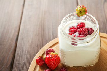 Milk yogurt in a jar with fresh raspberries and strawberries on a round wooden board