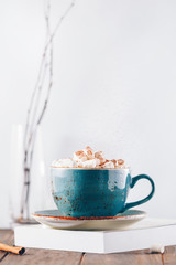 Obraz na płótnie Canvas Hot chocolate with marshmallows and cinnamon stick in a blue ceramic cup on a table with a book. The concept of winter or fall time. Minimal scandinavian design.