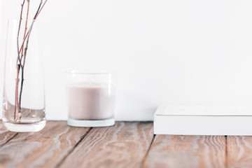 Wooden table with a candle, dead branches in a glass vase and a book near white wall. The concept of winter time. Background for text.