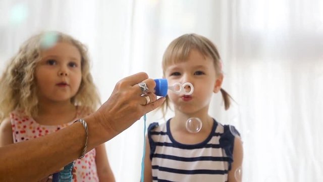 Cute little girl is blowing soap bubbles indoors. Slow Motion