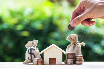 Saving money, home loan, mortgage, a property investment for future concept : A man hand putting money coin over small residence house and money bag.