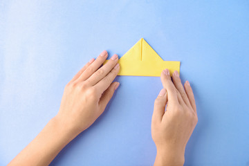 Woman making origami boat on color background