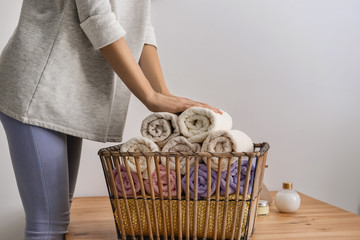 Woman folding clean soft towels into basket at wooden table
