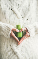 Winter seasonal smoothie drink detox. Female in warm sweater holding bottle of green smoothie or...