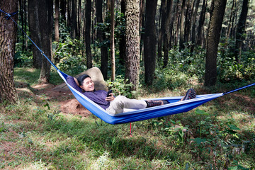 Handsome asian man using mobile phone while relaxing on the hammock