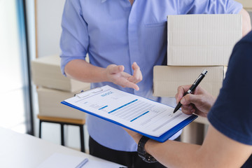 Young man signing invoice bill from delivery man after receiving parcel from courier at home. Delivery service concept