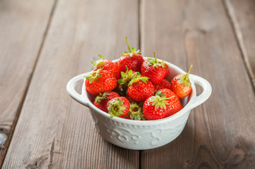 White plate with fresh ripe juicy strawberries on a wooden textural table close up