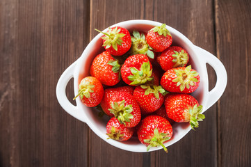 White plate with fresh ripe juicy strawberries on a wooden textural table close up