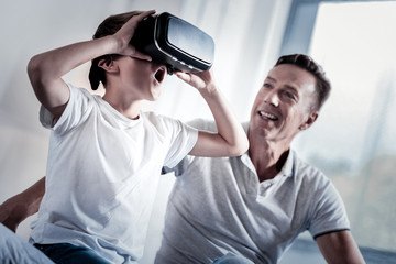 New experience. Amazed little surprised boy sitting in the bright room near his father examining...