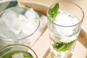 Glass of fresh cucumber water with ice cubes on tray, closeup