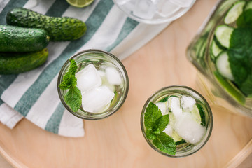 Glass of fresh cucumber water with ice cubes on tray