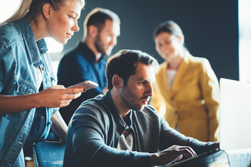 Startup and millenial business concept. Woman with mobile phone helps man with laptop to finish his daily plan
