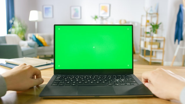 First Person Close-up Shot Man Uses Laptop With Green Mock-up Screen While Sitting At The Desk In His Cozy Living Room.