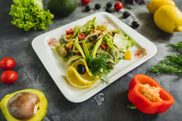 Salad with fresh vegetables, avocado, lemon on grey table.Tasty food