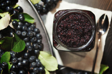 Jam from black chokeberries ( Aronia melanocarpa ) and its berries on dark table. Homemade preserves. Top view. Horizontal.